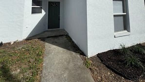 Una casa blanca de un piso con puerta principal, un porche pequeño y una ventana.