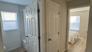 Un pasillo con un baño a la izquierda, un dormitorio a la derecha y una puerta en el centro.