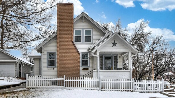 Une maison à deux étages, avec une façade blanche, une cheminée marron et une clôture blanche faite de piquets.