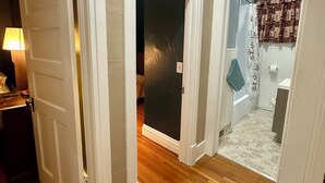 Un couloir au plancher de bois menant à une salle de bain avec des rideaux à motifs et des toilettes.