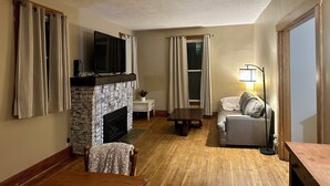 Un salon avec une cheminée, un téléviseur, un canapé, une table et une lampe.