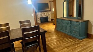Un coin repas avec une table et des chaises en bois, une commode bleue avec un miroir et un luminaire suspendu.