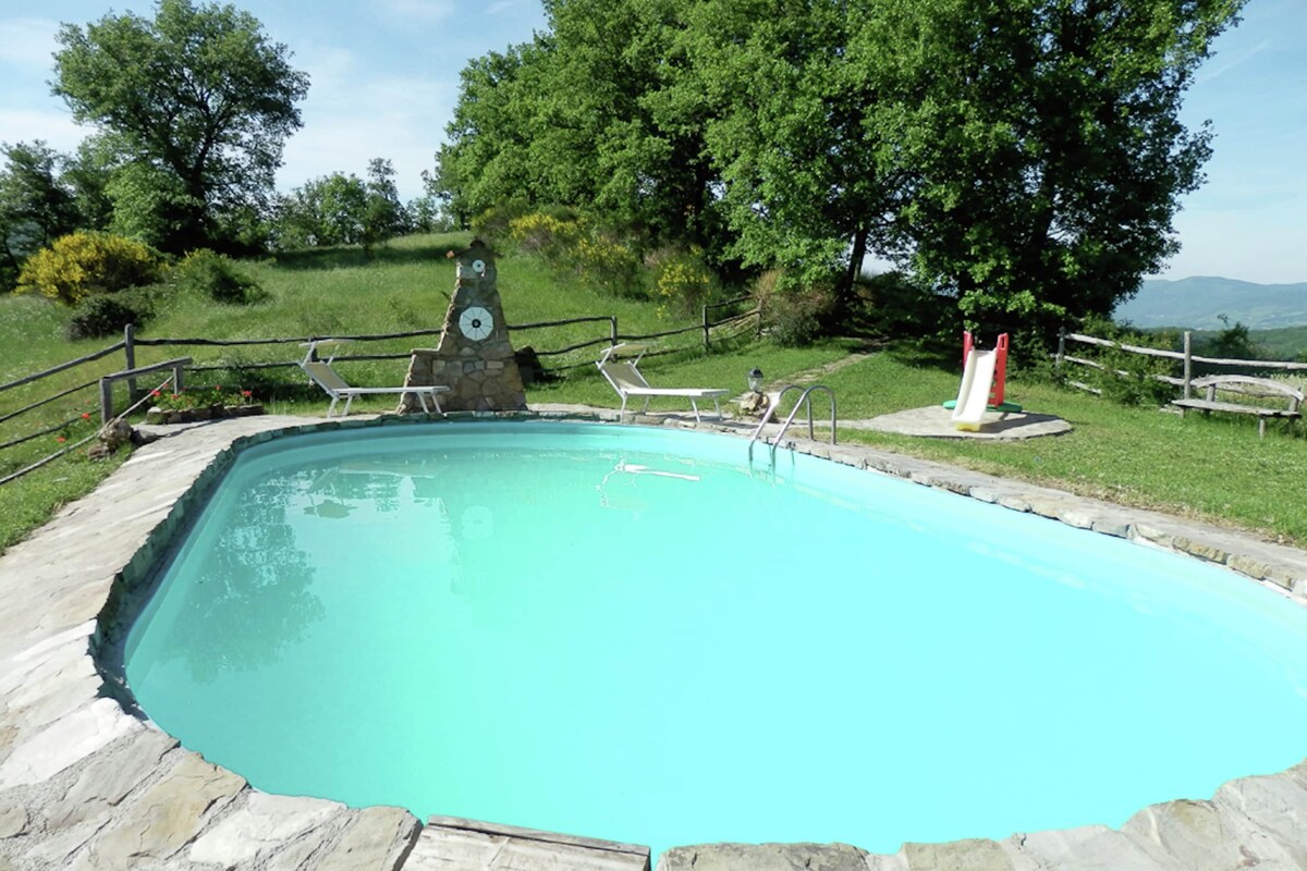 A rectangular swimming pool with a stone border, surrounded by a wooden deck and a stone wall.