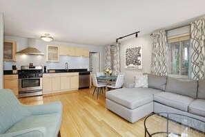 A modern living room with a grey sectional sofa, a light blue armchair, a glass coffee table, and a dining area with a glass table and chairs. - Cozy Condo in West Highlands quiet historic neighborhood. Home away from home! (Denver)