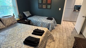 A bedroom with two beds, a small table, and a doorway leading to a kitchen. - Charming 2-bedroom apartment in superb Bennington with WiFi (Bennington)