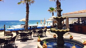 Un patio frente a la playa con palmeras, una fuente y mobiliario para exteriores.
