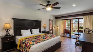 Una habitación de hotel con una cama grande, dos mesitas de noche con lámparas, un ventilador de techo y vistas del patio exterior.