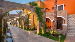 Un patio con arcos de piedra, un sendero y un edificio de paredes naranjas y fachada de piedra.