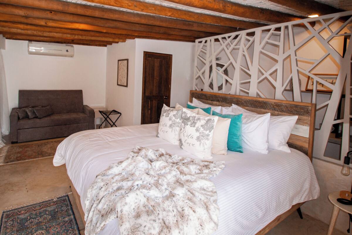A bedroom with a large bed, a wooden headboard, a brown sofa, and a patterned rug.