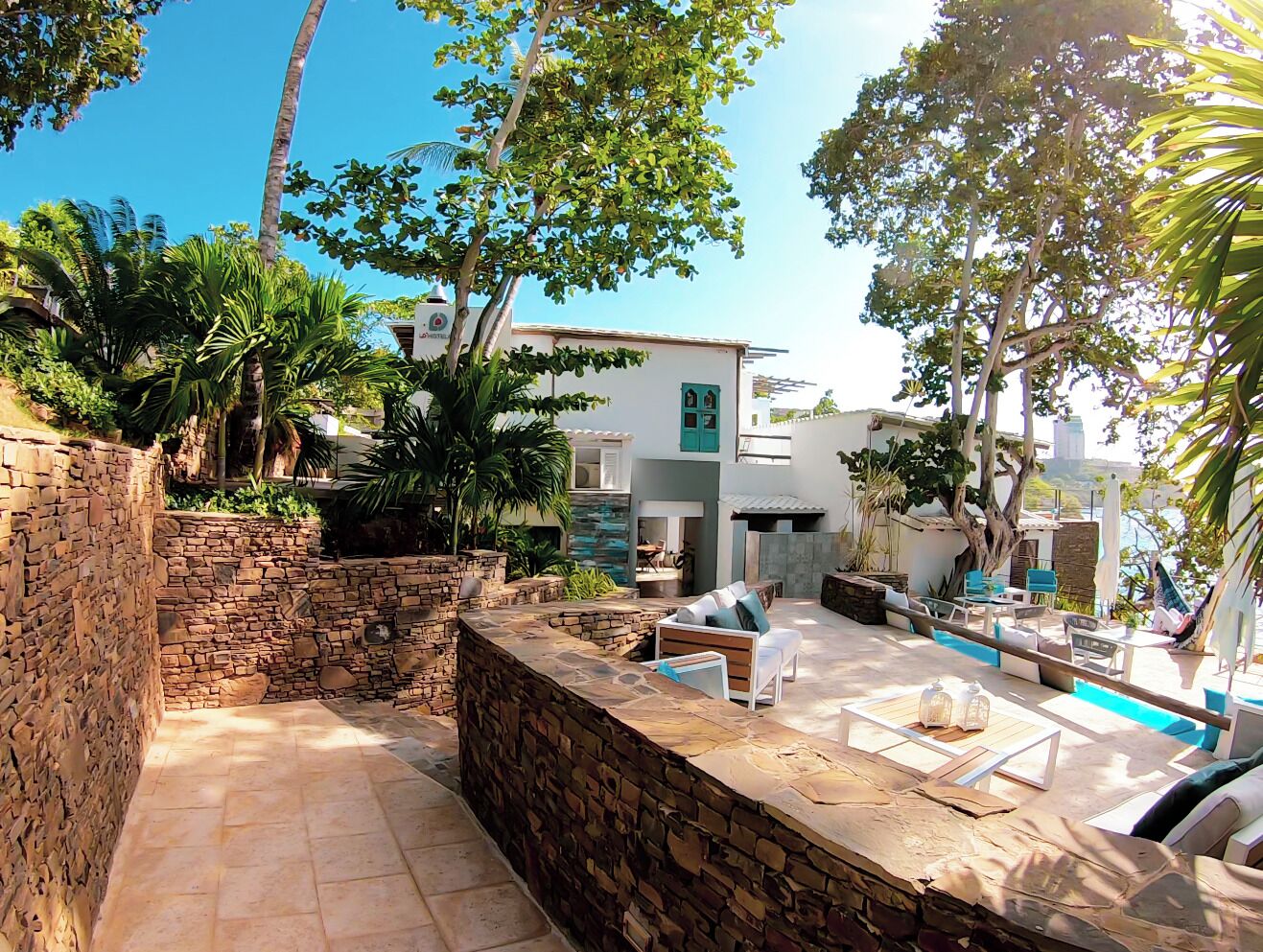 A stone-walled outdoor area with a pool, lounge chairs, and a building with a green window.