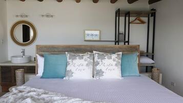 A bedroom with a bed, bedside tables, a mirror, a hanging light, a framed picture, and a bunk bed in the background.