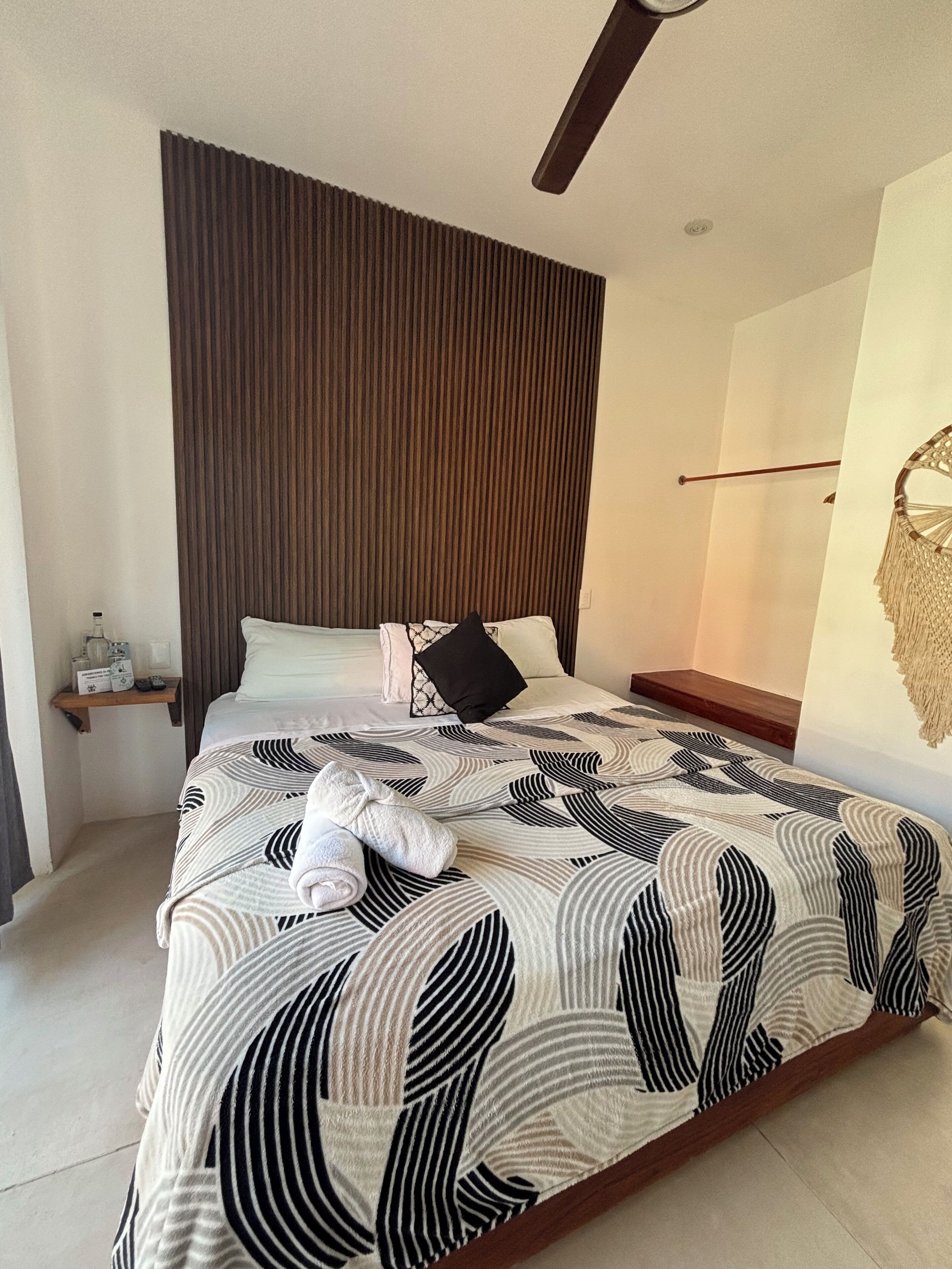 A modern bedroom with a large bed, a wooden headboard, a bedside table with a lamp, and a wall-mounted decorative piece.