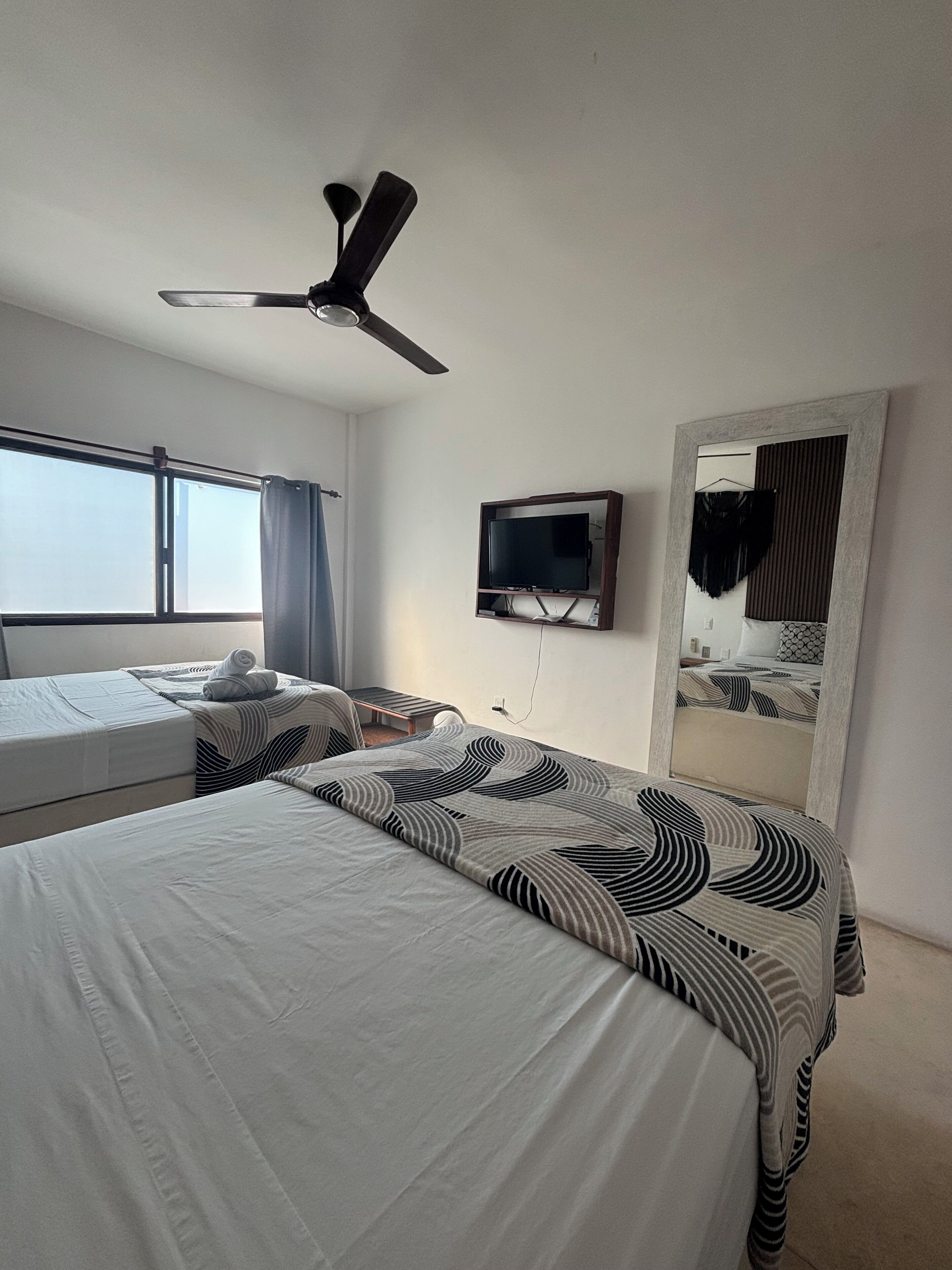 A hotel room with two beds, a ceiling fan, a TV, and a large mirror.