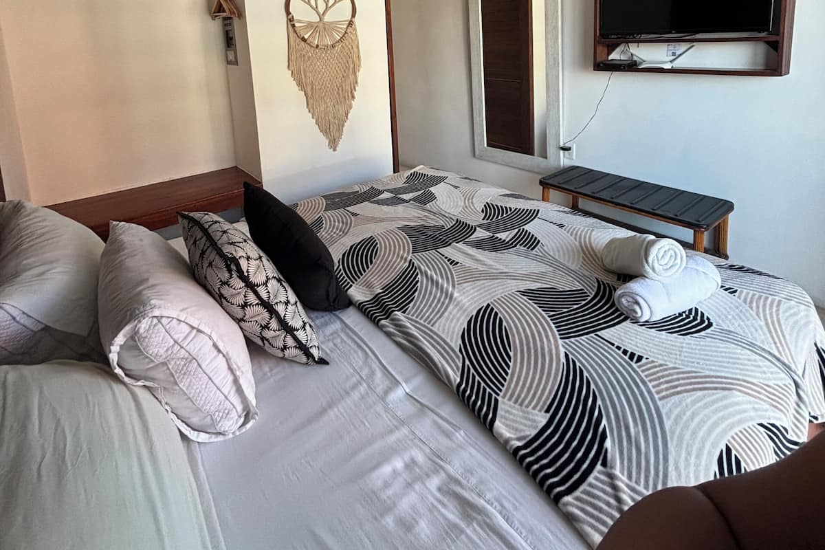 Une chambre à coucher comprenant un lit, un ventilateur de plafond, un téléviseur fixé au mur et une décoration murale en macramé.