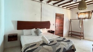 Une chambre d’hôtel avec un grand lit, une tête de lit en bois, une armoire en bois, un radiateur et un ventilateur de plafond.