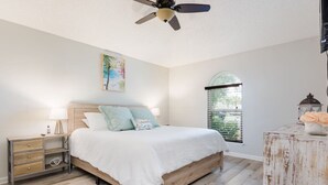 A bedroom with a wooden bed, a nightstand, a ceiling fan, a window with a view, and a decorative lantern. - Entire JAX Beach Bungalow 7 blocks from Ocean (Jacksonville Beach)