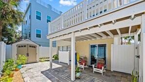 A covered patio area with a white pergola, a small seating area with a bench and a table, and a door leading to a garage.