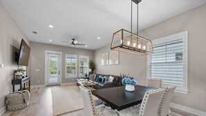 A dining area with a dark wooden table, beige upholstered chairs, and a modern pendant light.
