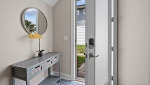 A hallway with a grey console table, a round mirror, and a door leading outside.