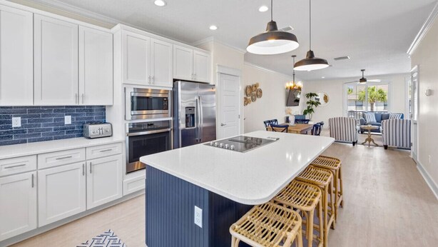 A modern kitchen with white cabinets, a large island, stainless steel appliances, and a dining area with striped chairs and a table. - *Brand New* Family Home, Steps From the Sand (Jacksonville Beach)