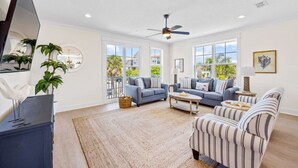 A spacious living room with a large TV, two sofas, a coffee table, and a striped armchair. - *Brand New* Family Home, Steps From the Sand (Jacksonville Beach)