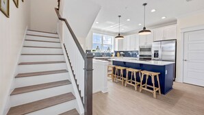 A modern kitchen with a central island, bar stools, and stainless steel appliances. - *Brand New* Family Home, Steps From the Sand (Jacksonville Beach)
