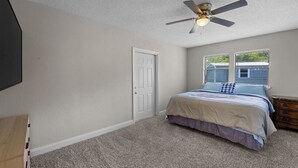 Ein Schlafzimmer mit Bett, Deckenventilator, Tür und Fenster mit Jalousien.