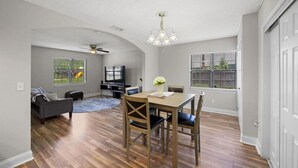 Ein geräumiges Wohnzimmer mit Essbereich, Deckenventilator und großem Fenster mit Jalousien.