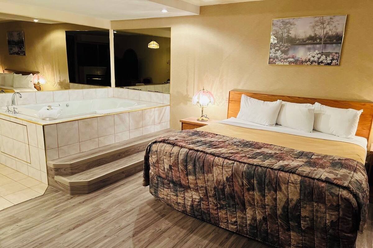 Ein Hotelzimmer mit einem großen Bett, einer Sitzecke inklusive Sessel, einem kleinen Tisch, einer Lampe und einem großen Spiegel.