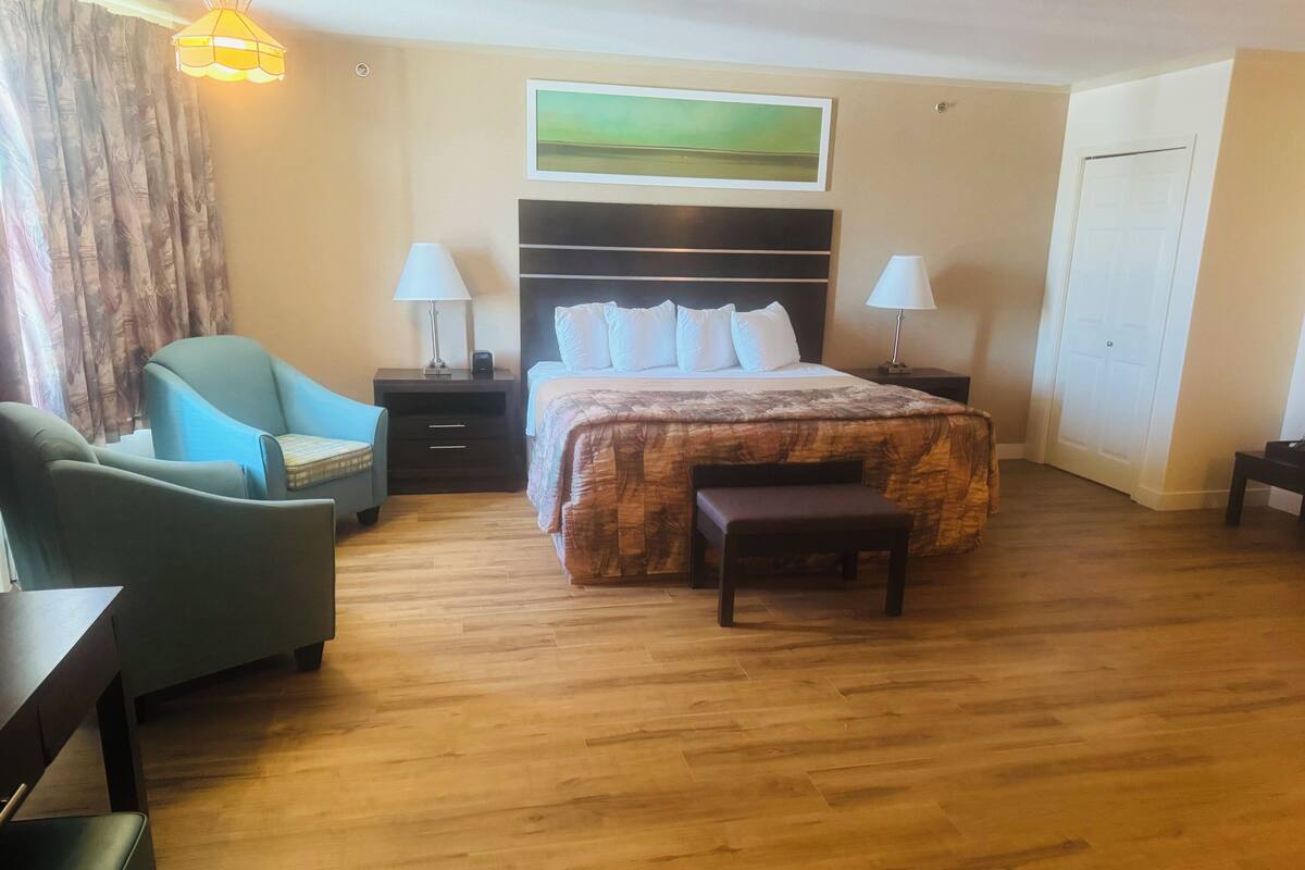 Ein Hotelzimmer mit einem Bett, zwei Nachttischen, einem Sessel, einer Bank, einer Lampe und einem Bild an der Wand.
