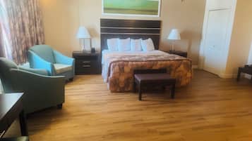 Une chambre d’hôtel avec un lit, deux tables de chevet, une chaise, un banc, une lampe et un tableau au mur.