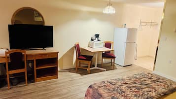 Habitación de hotel compacta con cama, escritorio, silla, televisor, microondas y refrigerador.