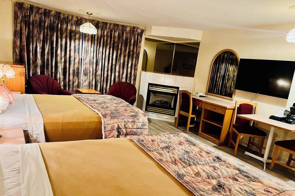 Ein Hotelzimmer mit zwei Betten, einem Schreibtisch, einem Sessel, einem Fernseher und einem Kamin.