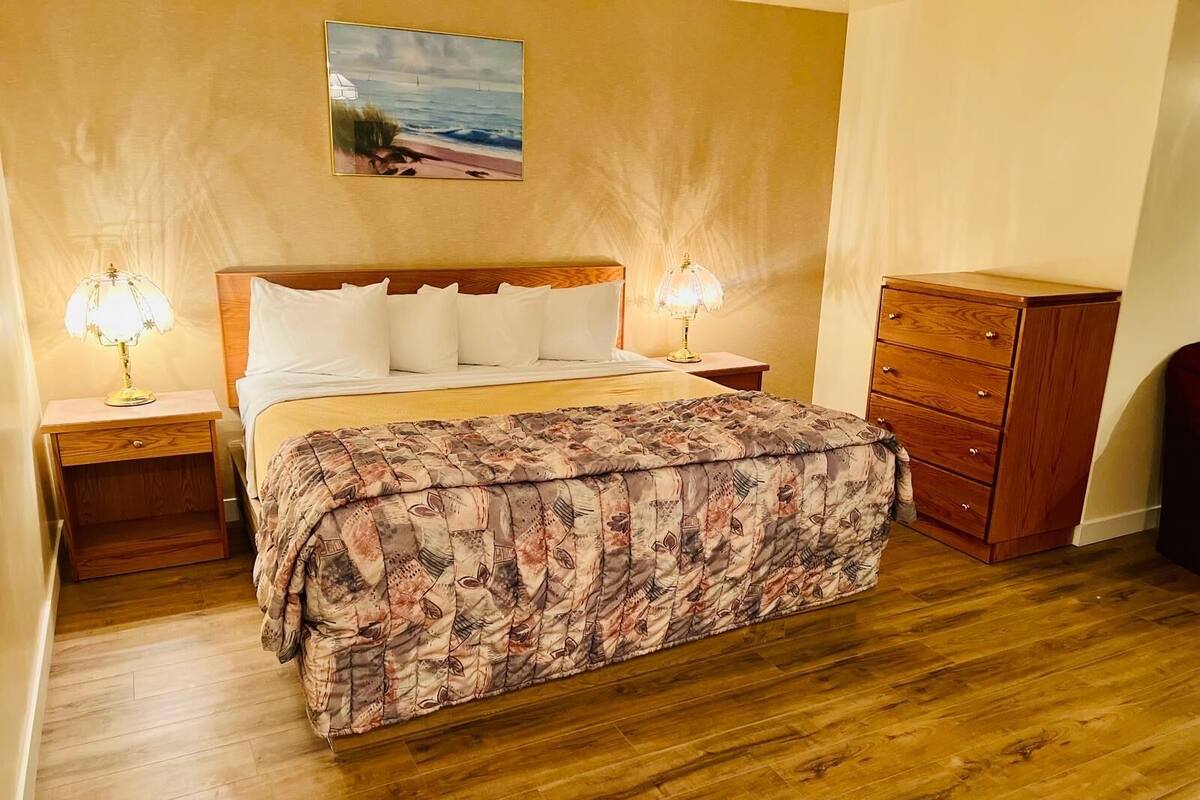 Ein Schlafzimmer mit einem Bett, zwei Nachttischlampen, einer Holzkommode und einem Bild einer Strandlandschaft an der Wand.