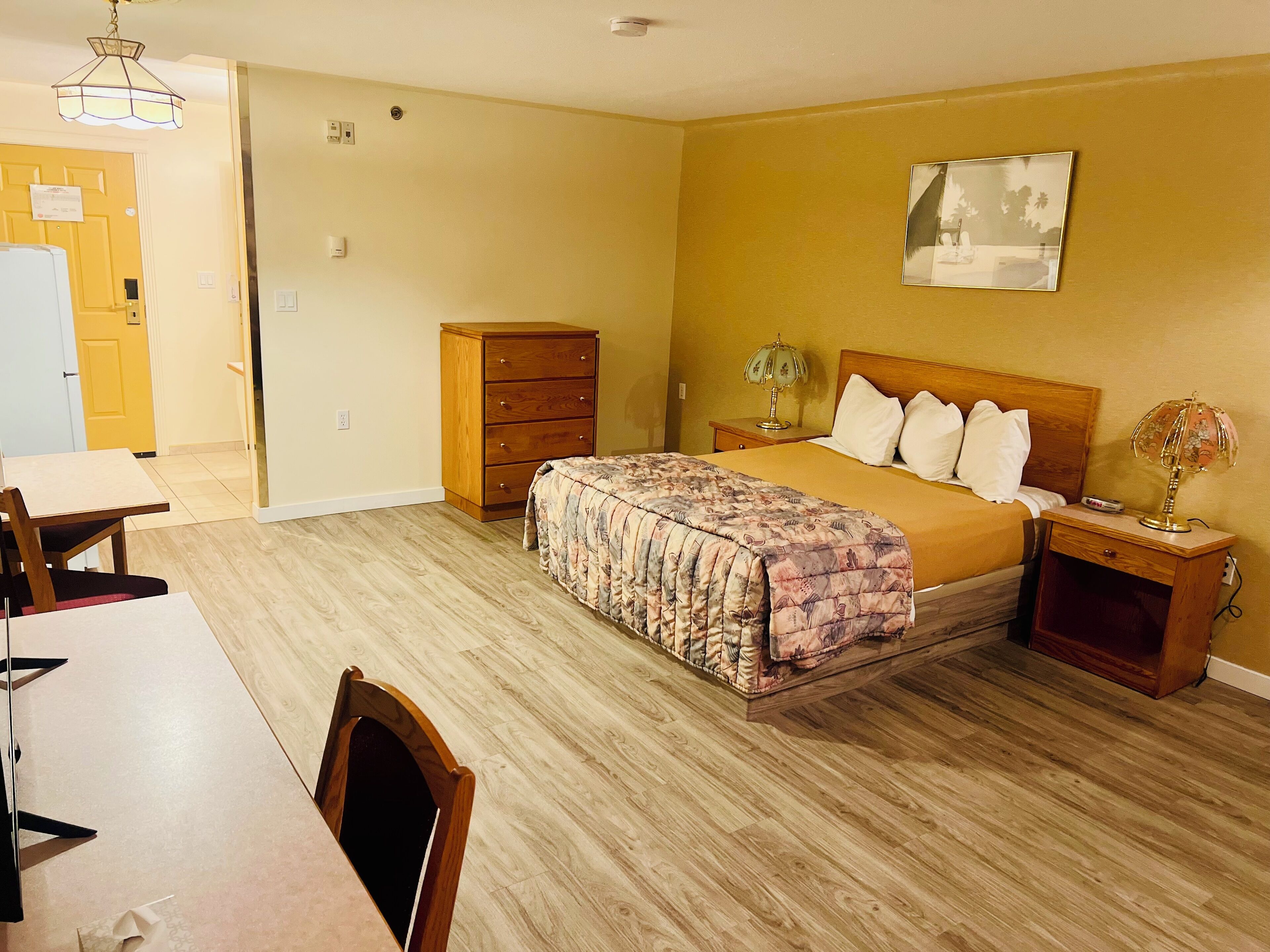 Un dormitorio con cama, mesita de noche, lámpara y cómoda de madera.