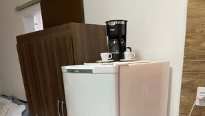Pieni, käytännöllinen keittiönurkkaus, jossa on jääkaappi, kahvinkeitin ja pieni liesi.
