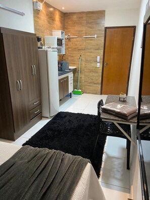 Een kleine hotelkamer met kitchenette, een behaarde zwarte vloerkleed, een bed en een houten deur.