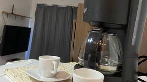 Kahvinkeitin pöydällä, sen vieressä kaksi valkoista kuppia ja aluslautasia.