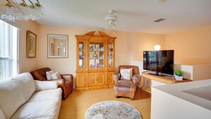 A living room with a white sofa, a brown leather armchair, a wooden cabinet, a television, and a ceiling fan. - Family Gem in Port St Lucie w/ Backyard & Pool! (Port St. Lucie)