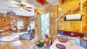 Interior acogedor de una cabaña con detalles de madera, un comedor, una cocina con estufa y utensilios, y un ventilador de techo.