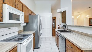 Una cocina moderna con electrodomésticos blancos, armarios de madera y encimera de mármol, con vista al área de estar contigua.