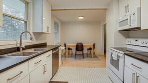 Et moderne køkken med hvide skabe, en stålvask, et træspisebord med fire stole og en indbygget ovn.