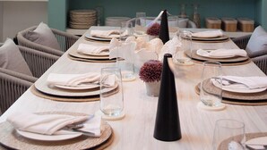 A dining area with a long table set for a meal, a hanging pendant light, and shelves with decorative items in the background. - Sabbia By LD Hoteles (Los Roques)