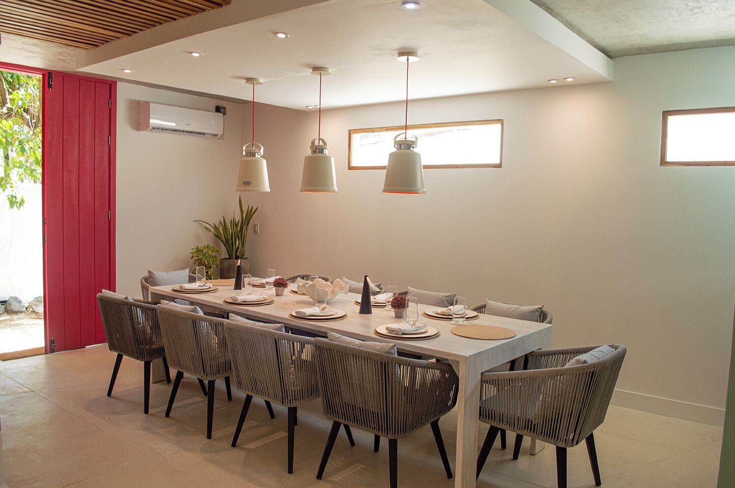 Un comedor moderno con una mesa larga, seis sillas de mimbre e iluminación colgante.