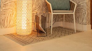A corner with a patterned wallpaper, a standing lamp, a chair, and a small table. - Sabbia By LD Hoteles (Los Roques)
