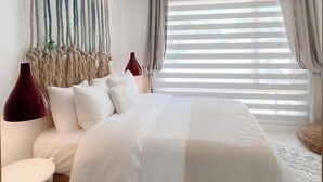 A modern bedroom with a large bed, a bedside table, a red lamp, and a macrame wall hanging. - Sabbia By LD Hoteles (Los Roques)