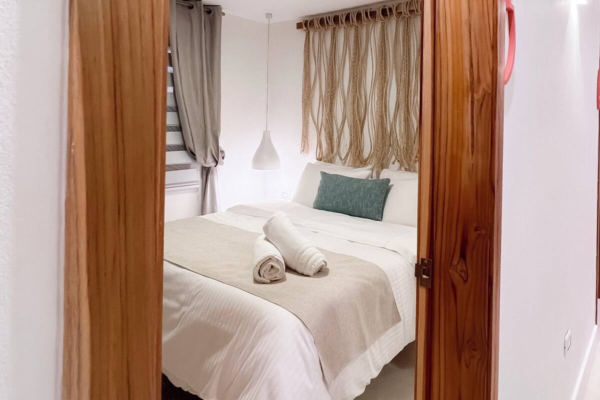 A bedroom with a bed, a hanging light, and a wooden door.