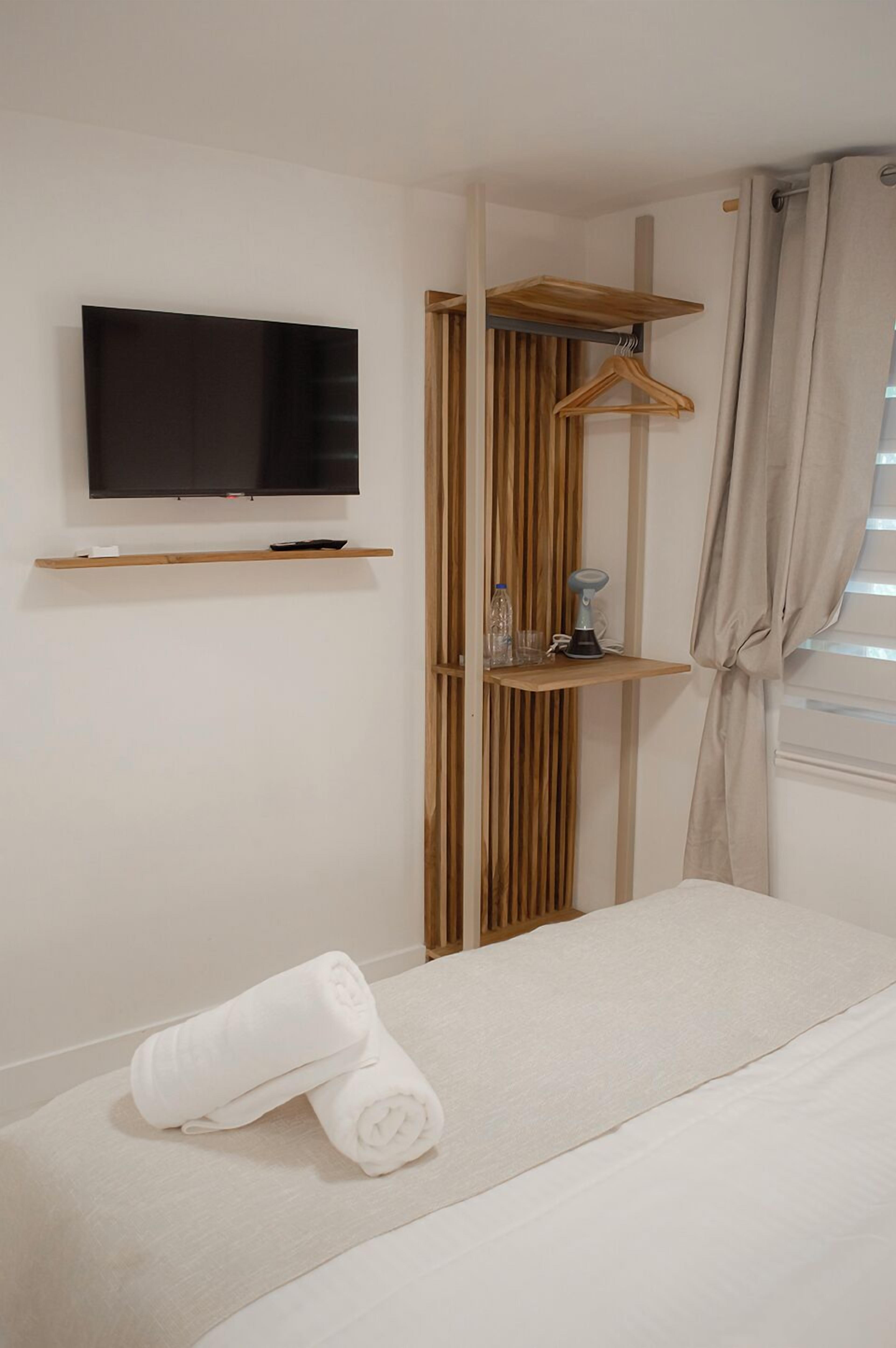 Habitación de hotel con cama, televisor montado en la pared, estanterías de madera y ventana con cortinas.