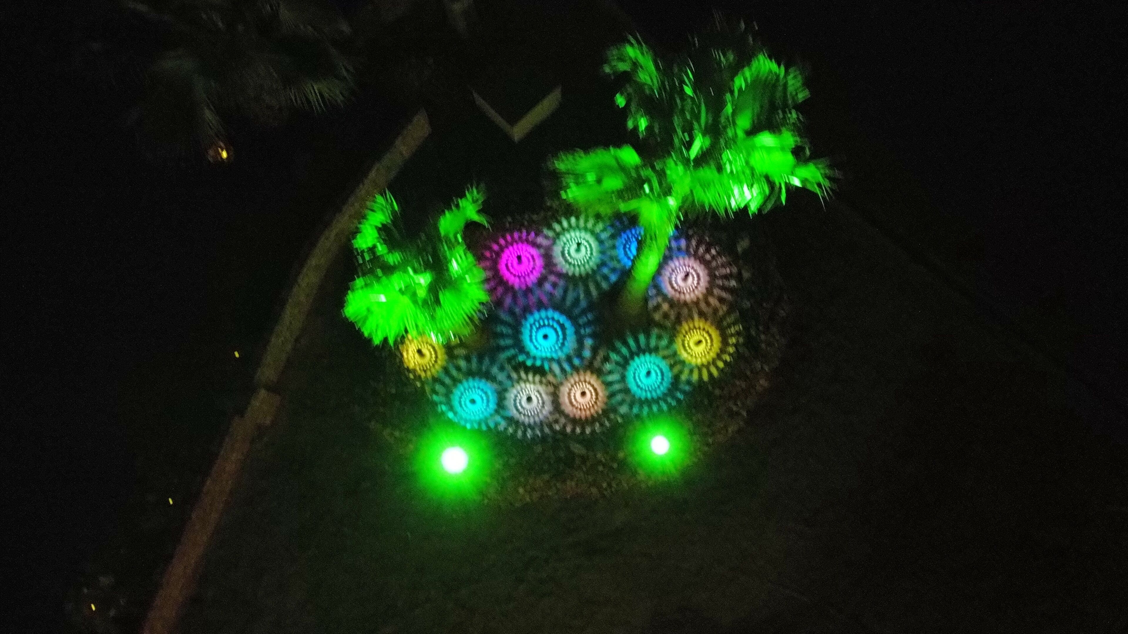 A dark outdoor area with a circular light installation featuring concentric circles in various colors.