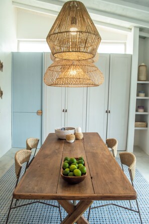 A dining table with a woven light fixture above it, surrounded by wicker chairs. - Laguna BY LD Hoteles (Los Roques)